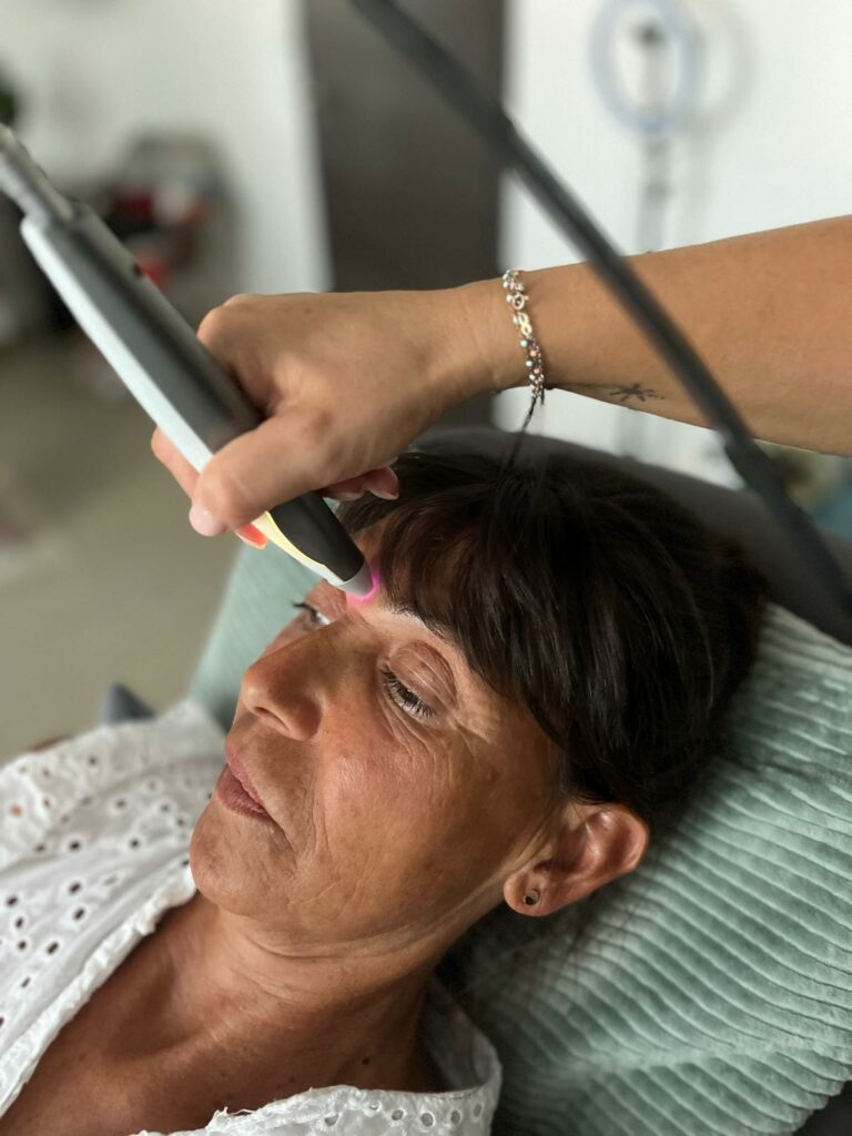 luxopuncture-front-relaxation-bien-etre Praticienne utilisant un appareil de luxopuncture sur le front d'une patiente, symbolisant relaxation, équilibre hormonal et soins non invasifs.
