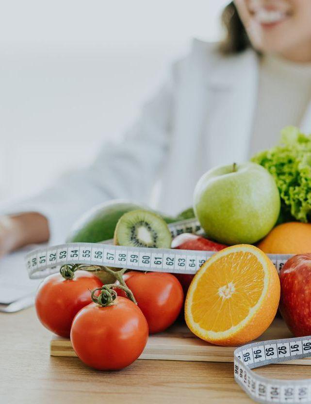 Fruits et légumes frais avec ruban de mesure, symbolisant une alimentation équilibrée et la gestion du poids dans un cadre diététique.