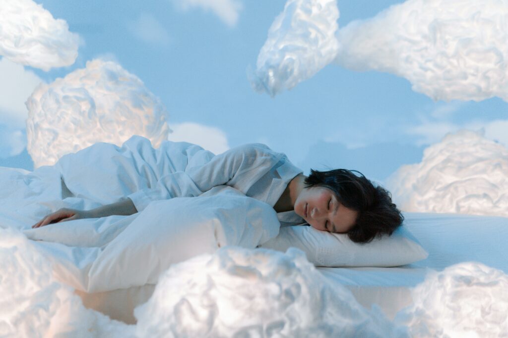 sommeil-reparateur-relaxation-et-serenite Femme endormie dans un décor onirique avec des nuages lumineux, symbolisant le bien-être, le sommeil réparateur et la détente profonde.
